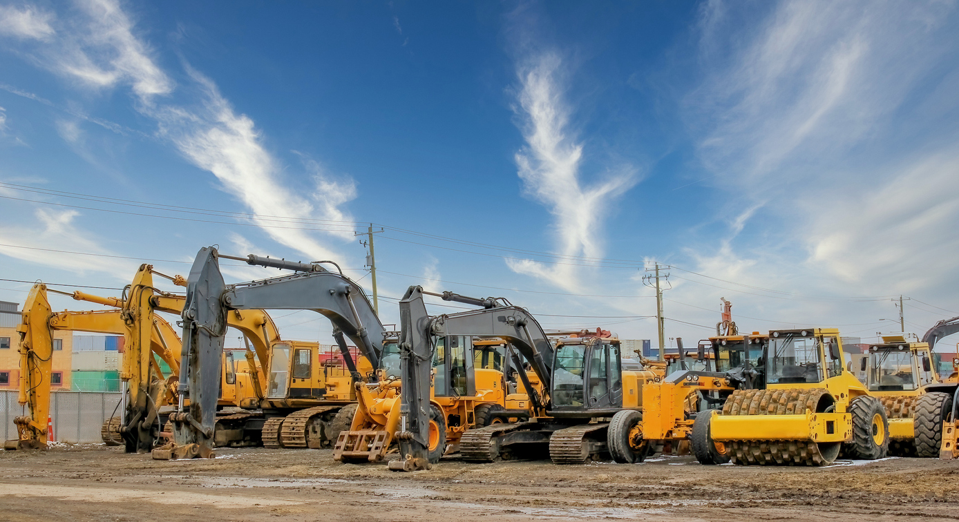 Row of excavators, bulldozers, and road rollers in a construction equipment yard